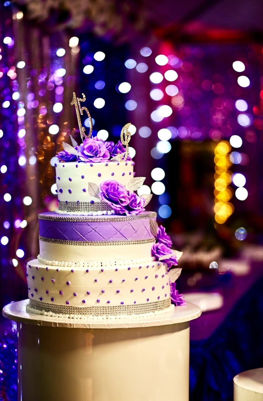 Pastel de XV años decorado con rosas moradas frente a las luces del salón